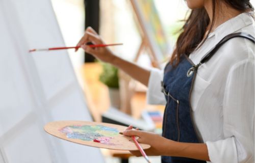 Mujer con pechera pintando en un atril con mezclador y pincel